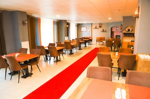 A hotel dining area with multiple tables and chairs, a red carpet, and a brick fireplace.