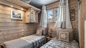 Une chambre confortable, aménagée dans le style d’un chalet, avec deux lits, des murs en bois, une fenêtre avec des rideaux et un tableau encadré accroché au mur.
