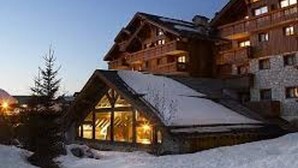 Un grand chalet en bois à plusieurs étages, doté d’un toit à forte pente, de grandes fenêtres et d’un terrain recouvert de neige.