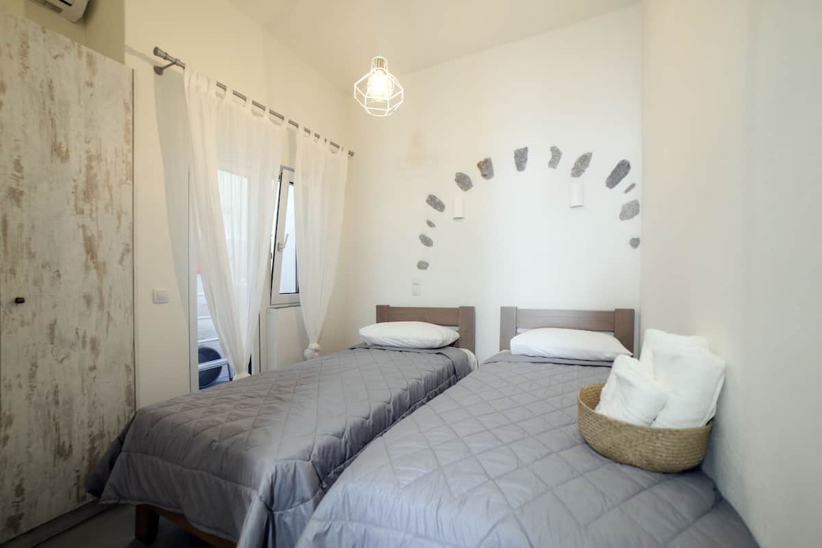 Ein Schlafzimmer mit zwei Betten, einem Fenster mit durchsichtigen Vorhängen, einer Wandleuchte und einer Steinmuster-Wand.