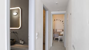 Un couloir étroit m ène à une chambre qui contient un lit, une table de chevet et un luminaire fixé au mur.