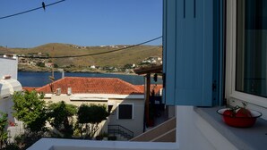 Un balcon donnant sur une ville côtière, un toit recouvert de tuiles rouges et un bol rouge posé sur le rebord de la fenêtre.