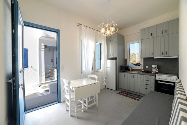 A compact kitchen with a dining area, a built-in oven, and a coffee maker. - Amphoras Apartments (Kea)