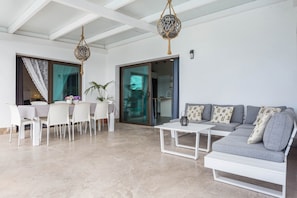 Un salon moderne comprenant un coin repas, un canapé gris, une table basse blanche et un luminaire suspendu.