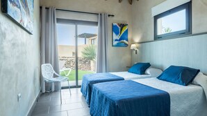 Habitación de hotel con dos camas, una puerta corrediza de vidrio a un patio, una silla y obras de arte en las paredes.