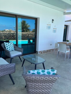 Ein Balkon mit Korbmöbeln, einem Glastisch und Blick auf einen Pool und die Landschaft.