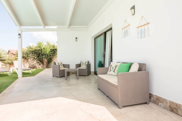 Eine überdachte Terrasse mit einer Couch, Stühlen und einem Tisch.