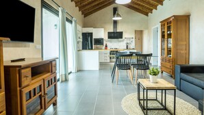Un salón amplio con techo de madera, televisor montado en la pared, una mesa de comedor con sillas y un sofá.