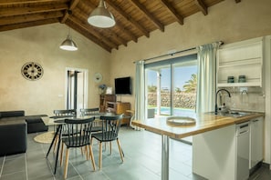 Une cuisine moderne avec un plafond en bois, un coin repas doté d’une table en verre et une vue sur une piscine.