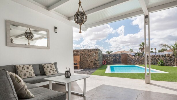 Ein modernes Wohnzimmer mit einem grauen Sofa, einem weißen Couchtisch und einem großen Fenster mit Blick auf einen Swimmingpool.