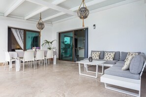 A modern living room with a dining area, a grey sofa, a white coffee table, and a hanging light fixture.