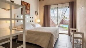 Ein Schlafzimmer mit Bett, Schreibtisch, Stuhl, einem Fenster mit Vorhängen und Blick ins Freie.