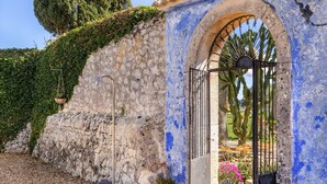 Un muro de piedra con una reja metálica, un arco pintado de azul y un cactus al fondo.