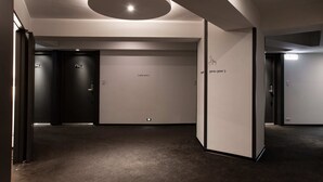 Un couloir moderne avec un luminaire circulaire, des portes portant des numéros de pièce et un sol recouvert de moquette.
