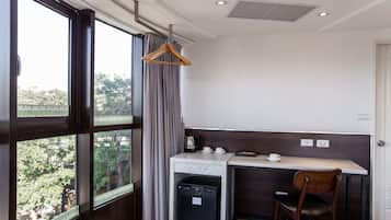 A compact room with a desk, a chair, a small refrigerator, and a hanging coat rack.