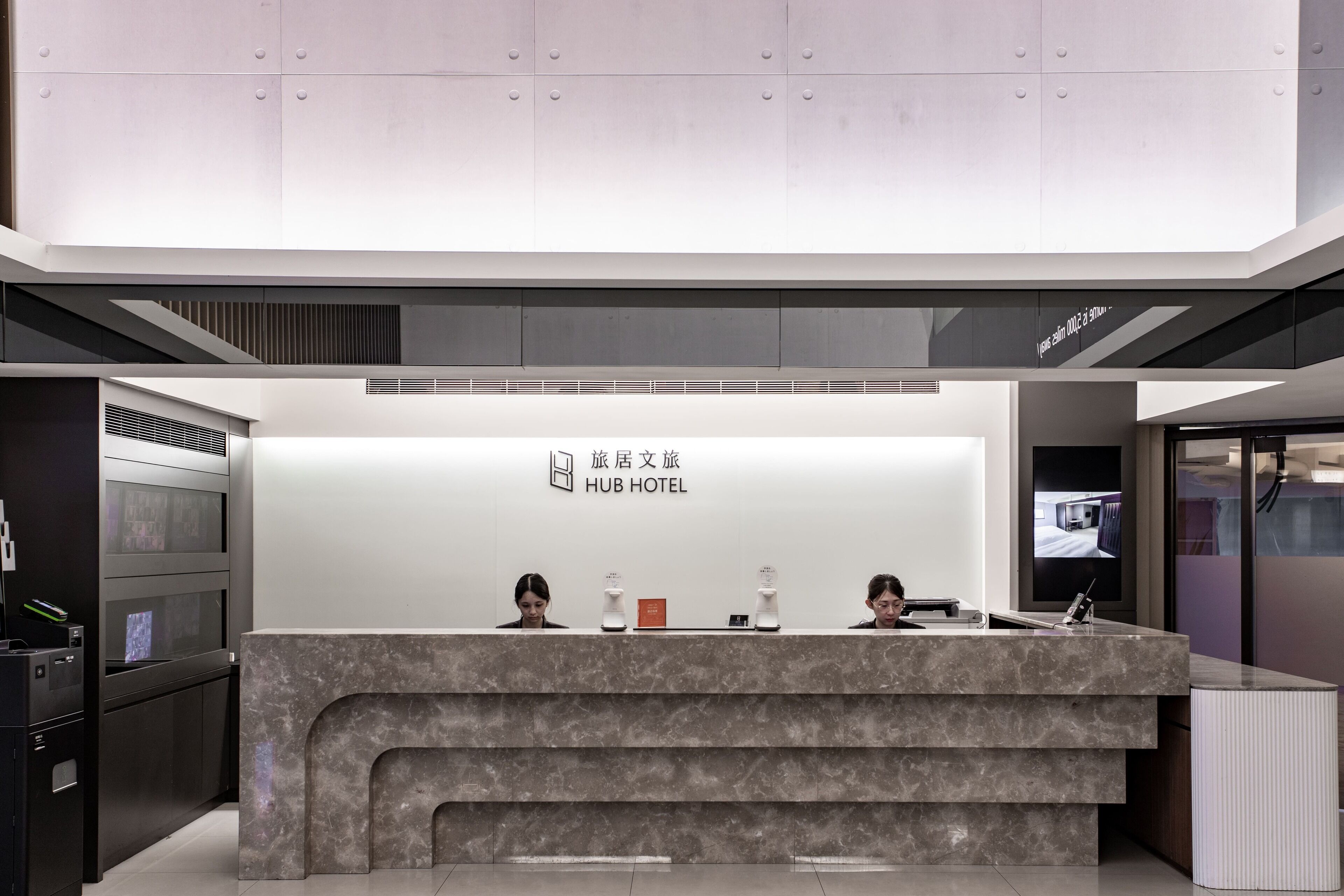 Un comptoir d’accueil moderne pour hôtel, doté d’un plan de travail en marbre, d’un écran numérique et d’une enseigne indiquant « HUB HOTEL ».