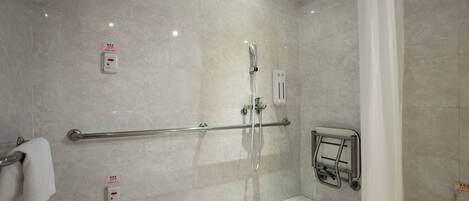 Une salle de bain moderne équipée d’une douche, de barres d’appui et d’un sèche-mains.