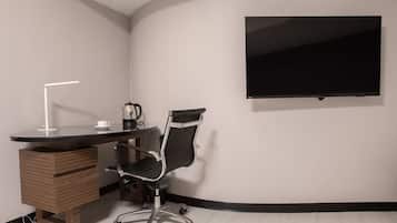 A modern office space with a curved desk, a black office chair, a flat-screen TV mounted on the wall, and a coffee maker on the desk.
