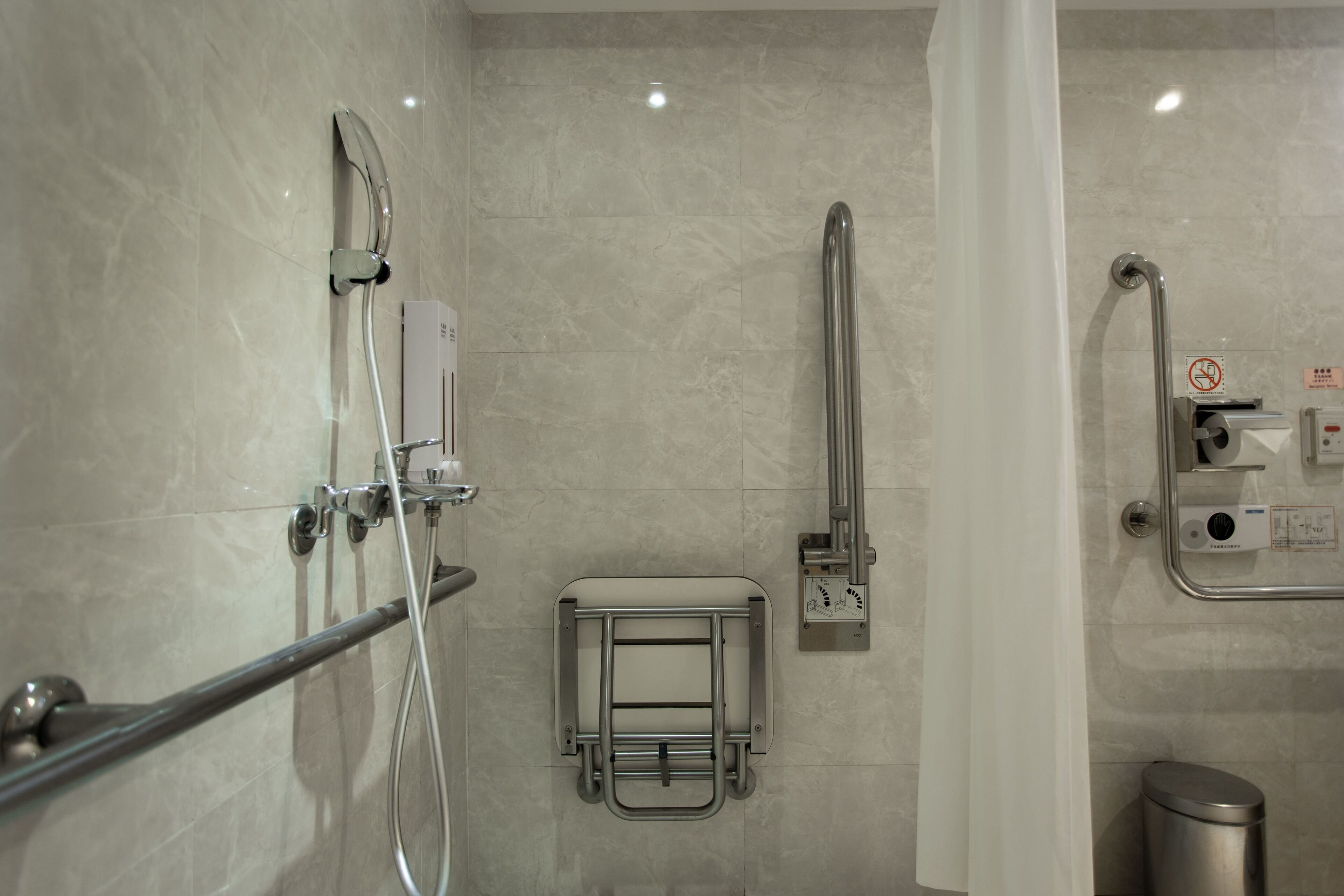 A modern bathroom with a shower, grab bar, and a hand dryer.