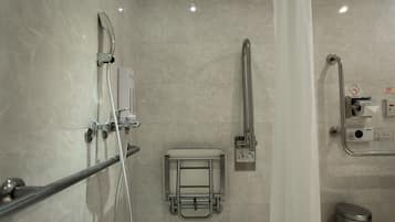 A modern bathroom with a shower, grab bar, and a hand dryer.