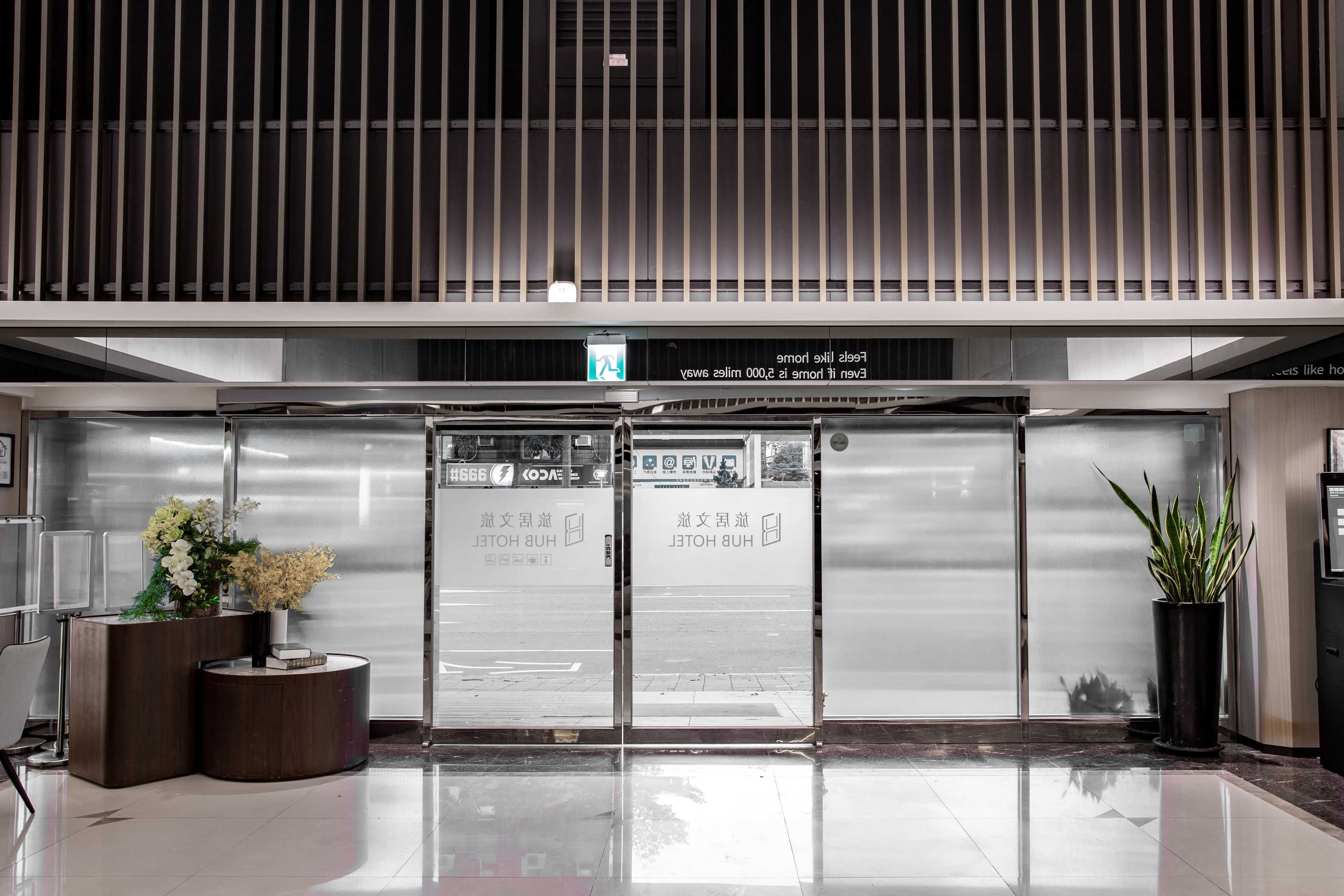 A modern hotel lobby with a reception desk, a glass door entrance, and a potted plant.