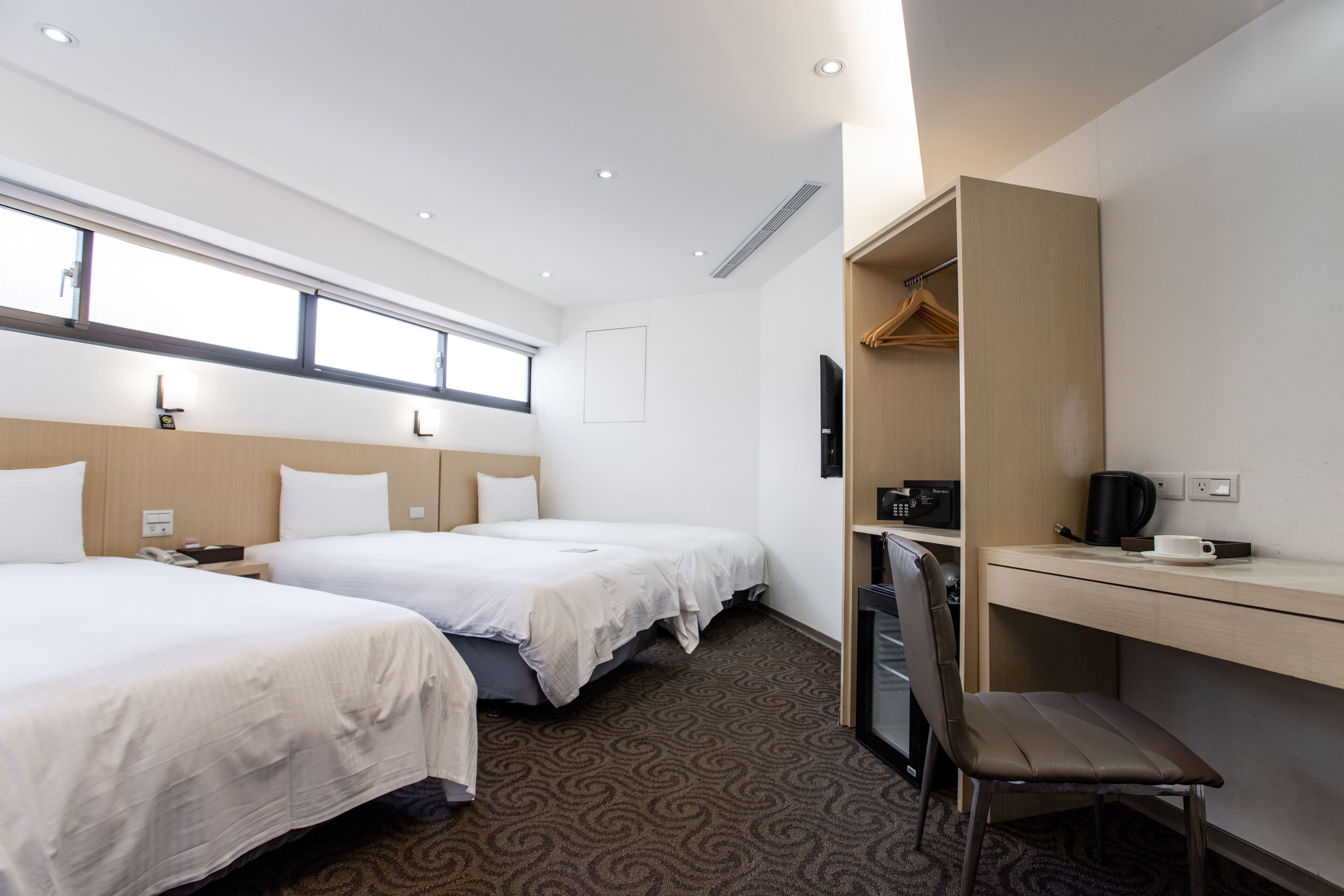Habitación de hotel con dos camas, un escritorio, una silla, un televisor y una ventana.