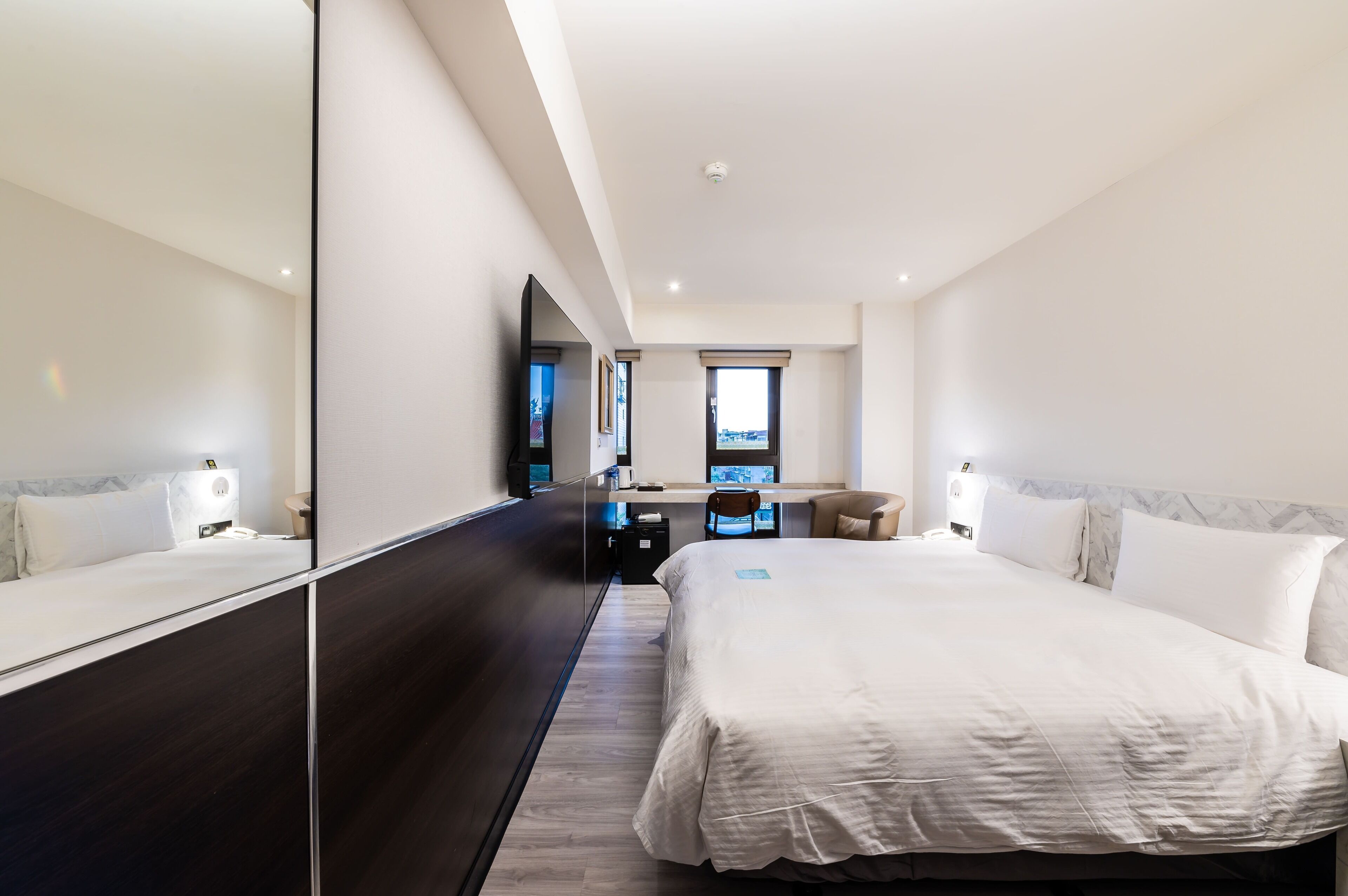 Habitación de hotel moderna con una cama grande, un escritorio, una silla y un espejo amplio.