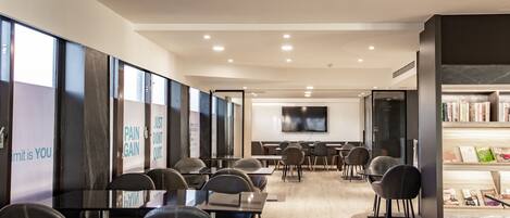 A modern conference room with glass walls, a flat-screen TV, and a bookshelf with magazines.