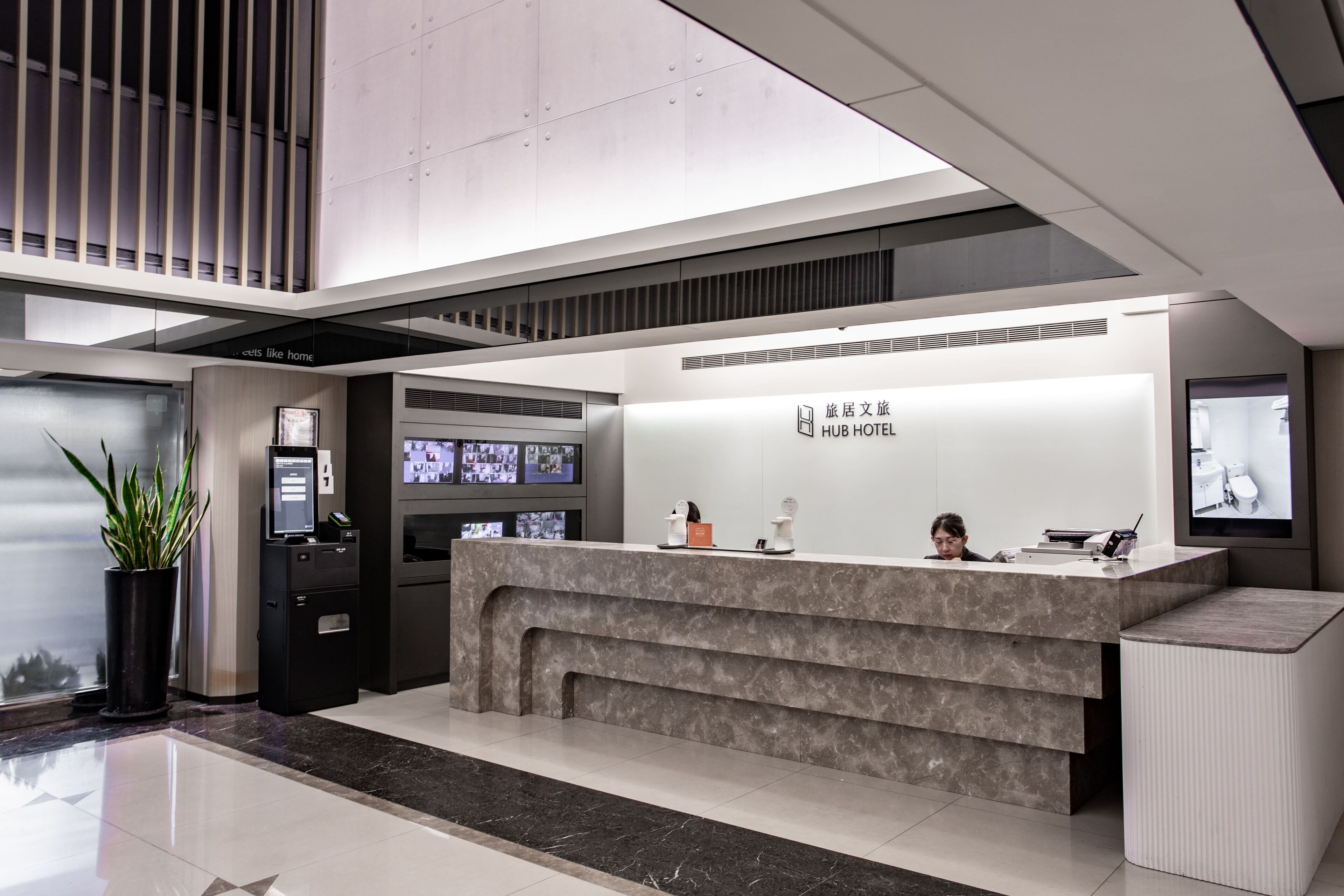 A modern hotel reception desk with a digital display, a seating area, and a large window.