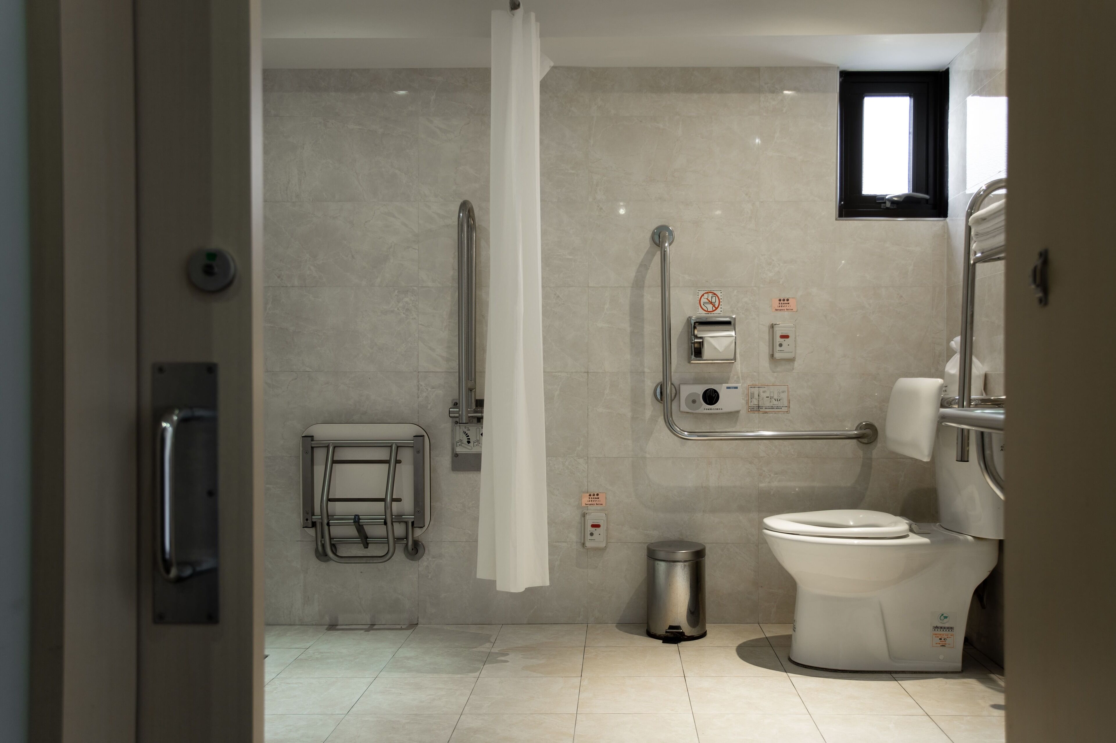 Une salle de bain moderne équipée de toilettes, d’une barre d’appui et d’une petite fenêtre.