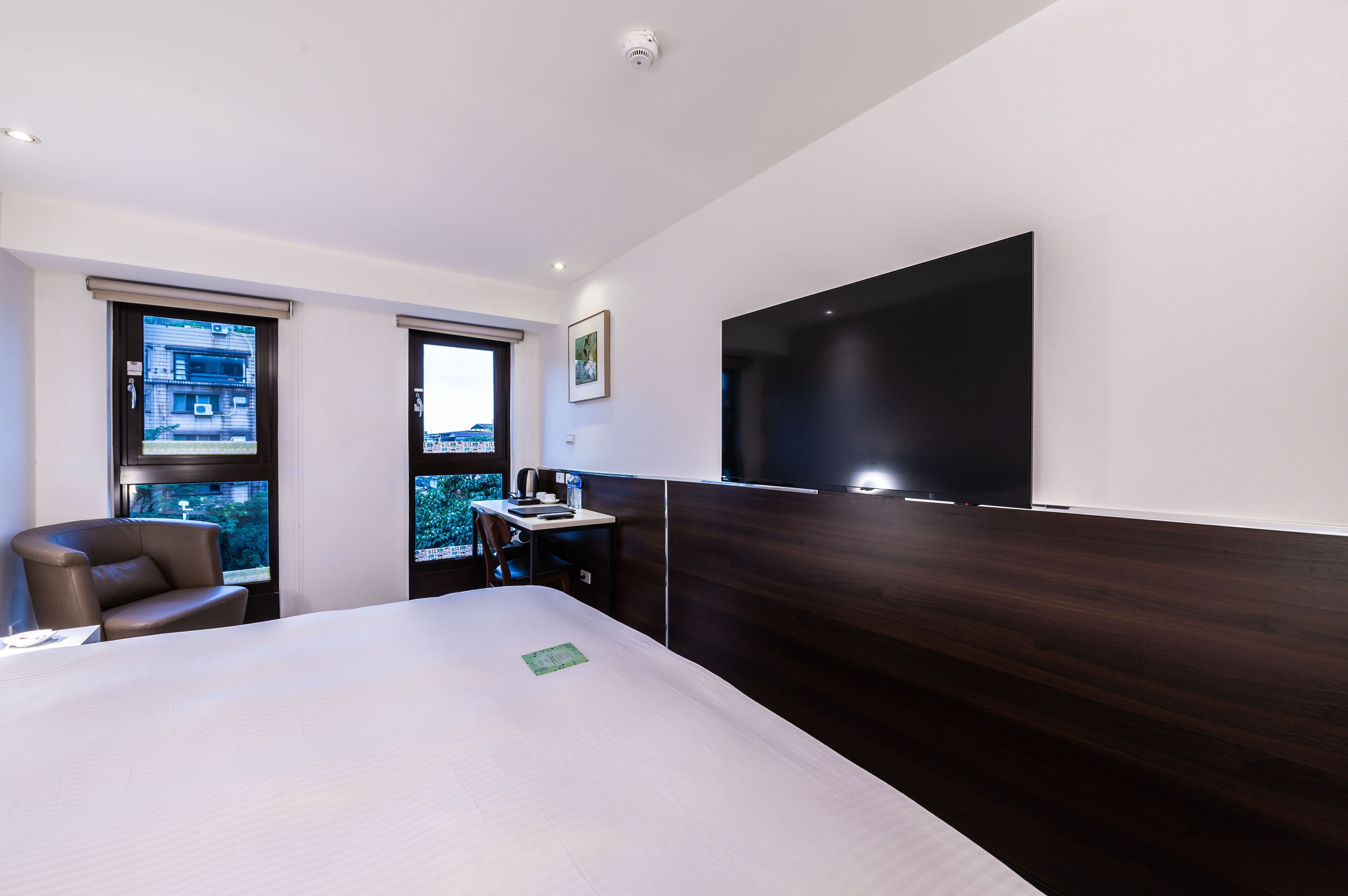 A modern hotel room with a large bed, a desk, a chair, and a TV mounted on the wall.