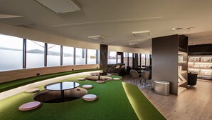 Un espace de détente moderne avec un gazon synthétique vert, des sièges disposés en cercle, une grande fenêtre donnant sur la mer et une bibliothèque remplie de livres.