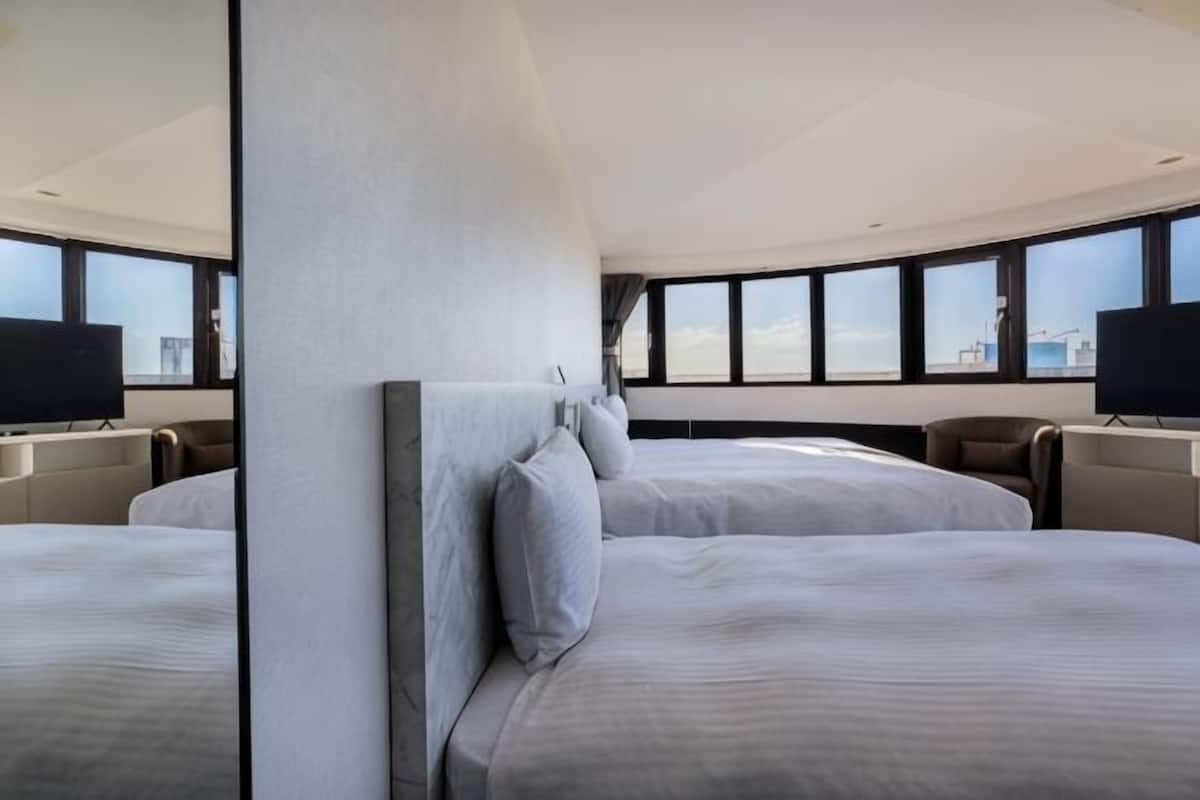 Habitació d'hotel amb dos llits, una finestra gran, televisió de pantalla plana i vista a la ciutat.