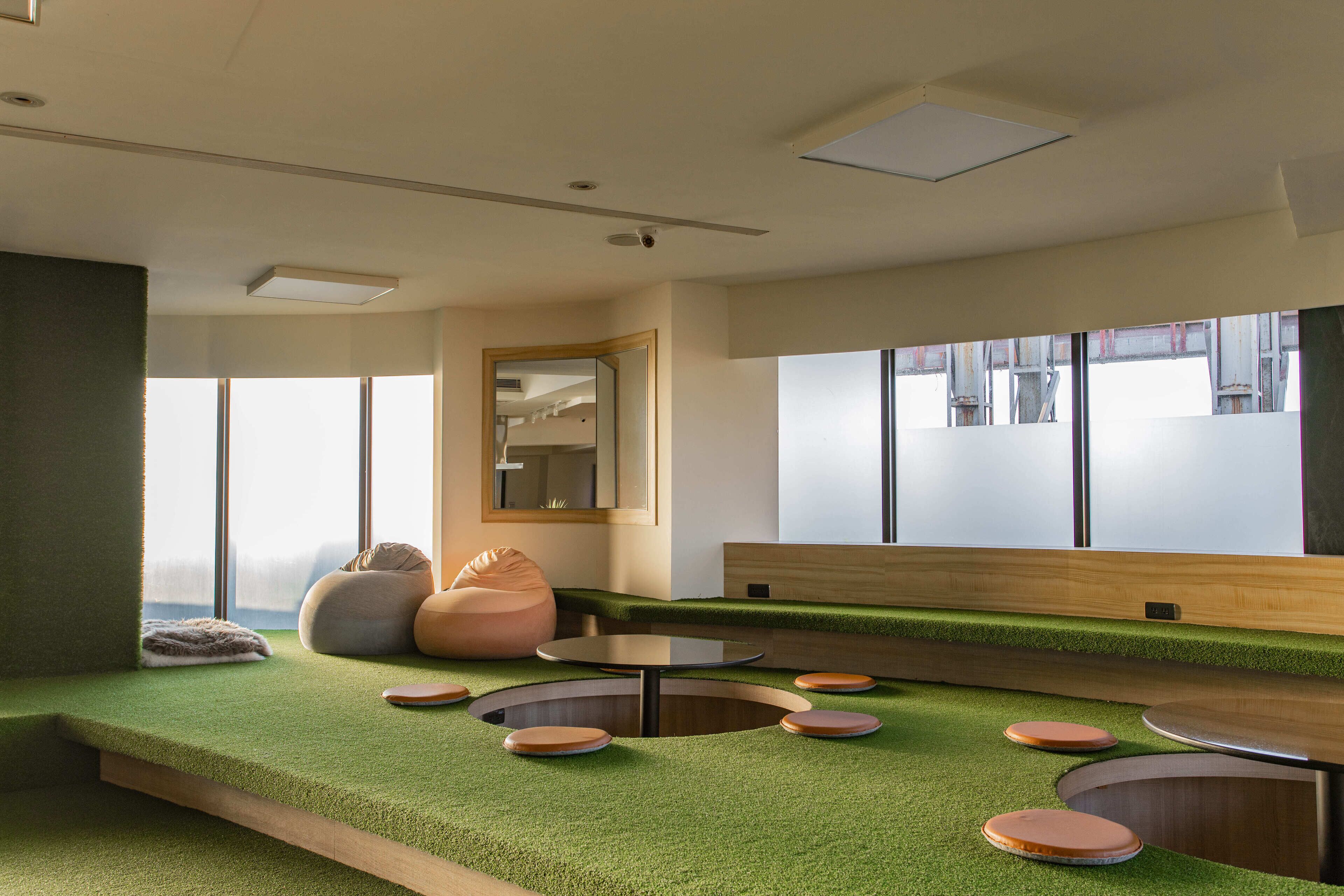 Een modern interieur met een vloer van kunstgras, ronde tafels en relaxstoelen.