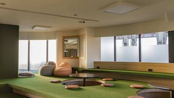 A modern interior with a green artificial grass floor, round tables, and bean bags.