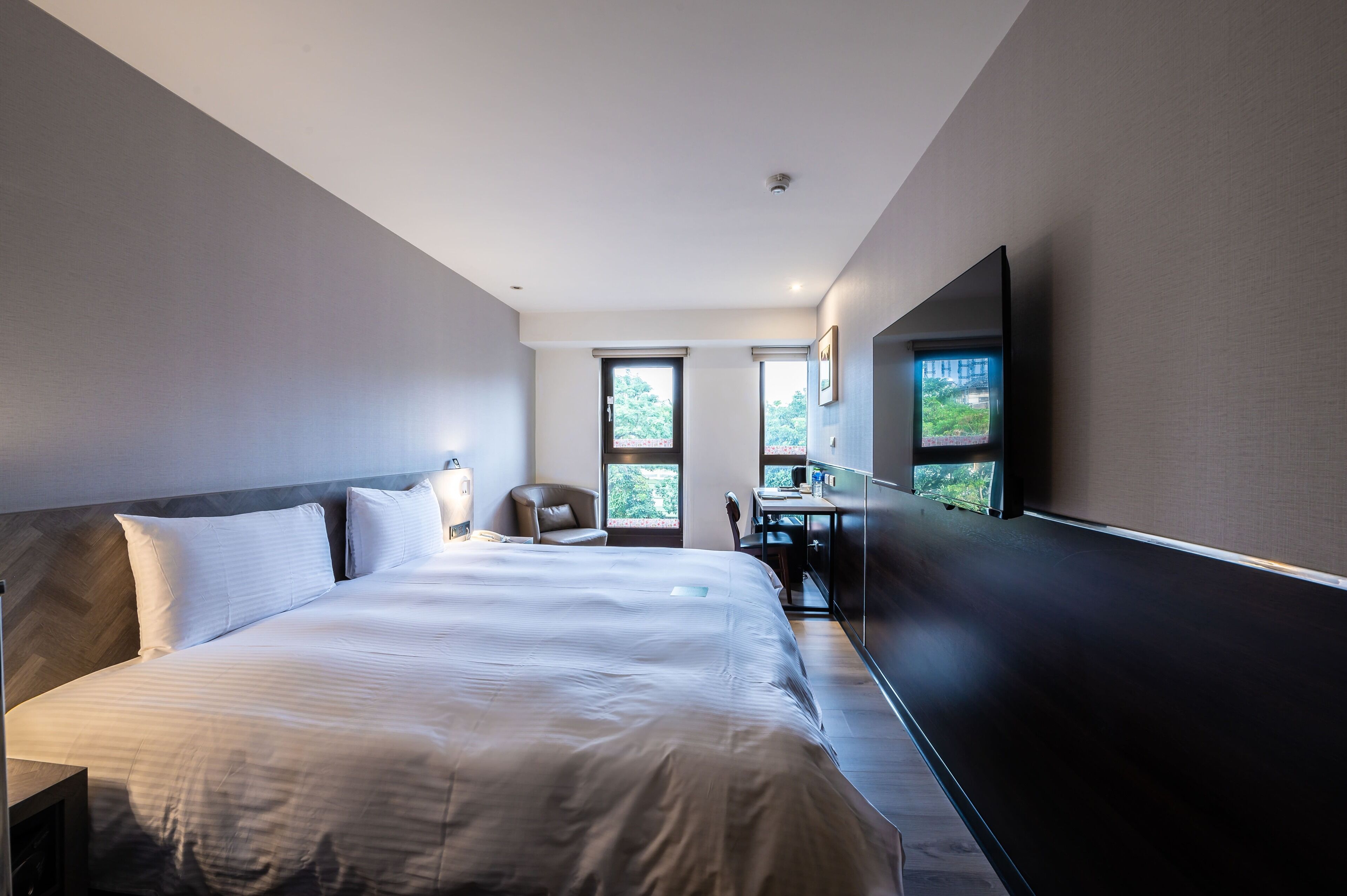 Une chambre d’hôtel moderne, dotée d’un grand lit, d’un bureau, d’une chaise et d’un téléviseur fixé au mur.
