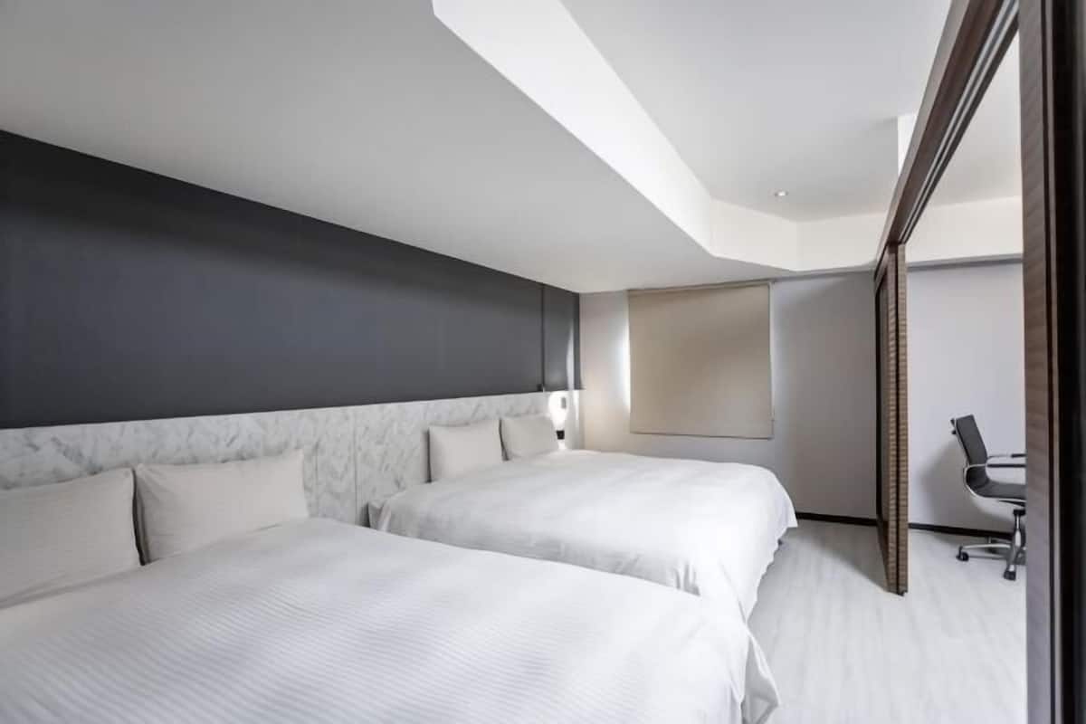 Habitació d'hotel moderna amb dos llits, un escriptori i un mirall gran.