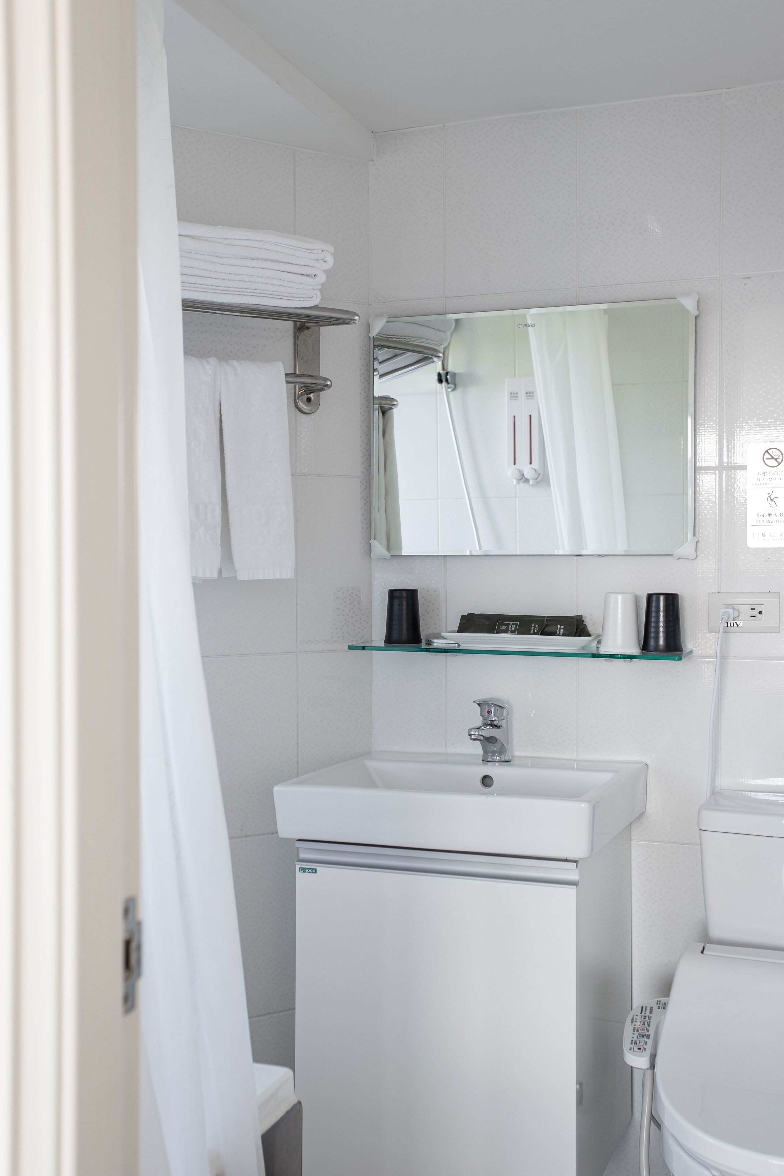 A modern bathroom with a white sink, a toilet, and a glass shelf above the sink.