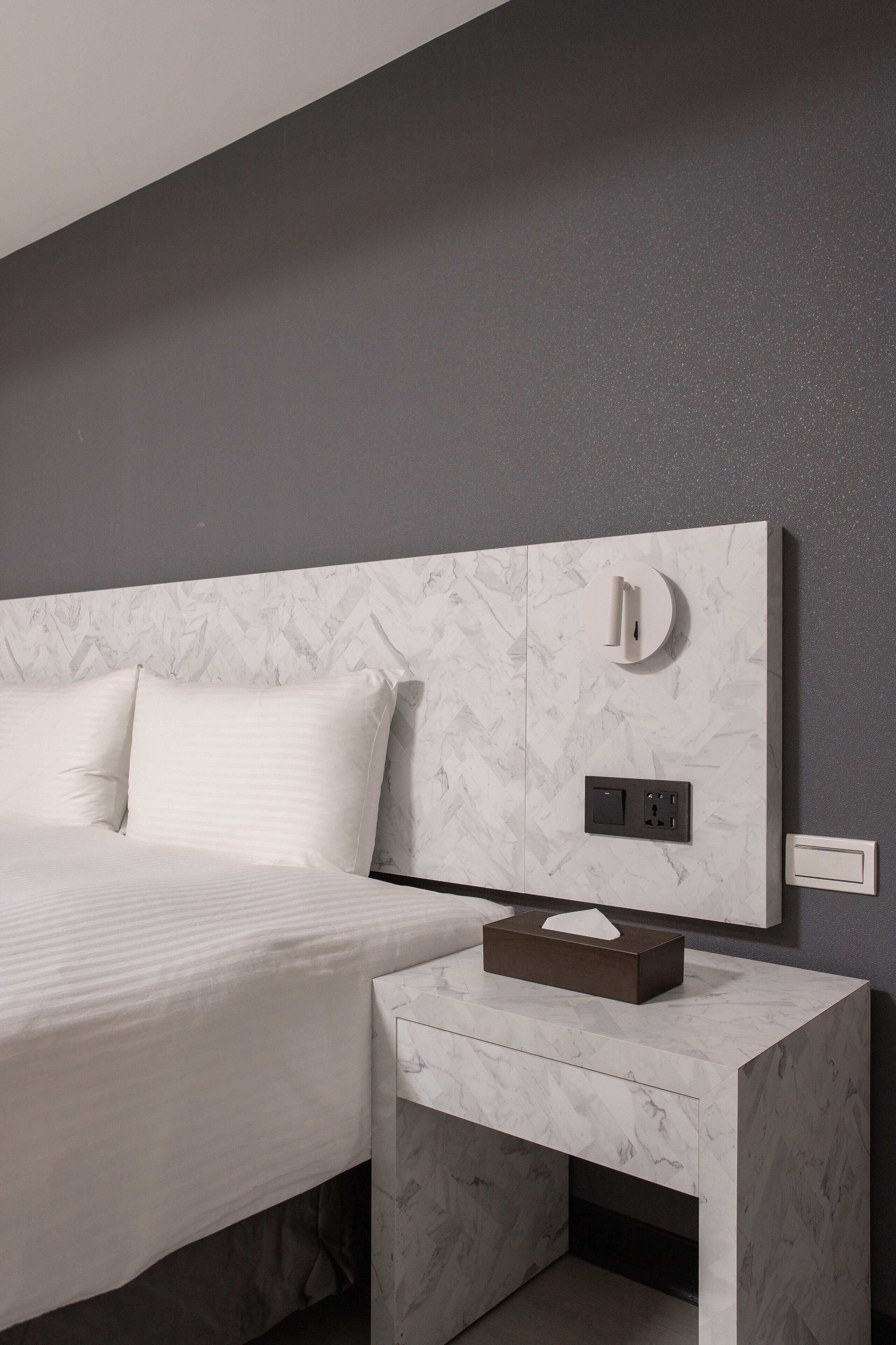 A modern hotel room with a marble headboard, a bedside table with a tissue box, and a power outlet.