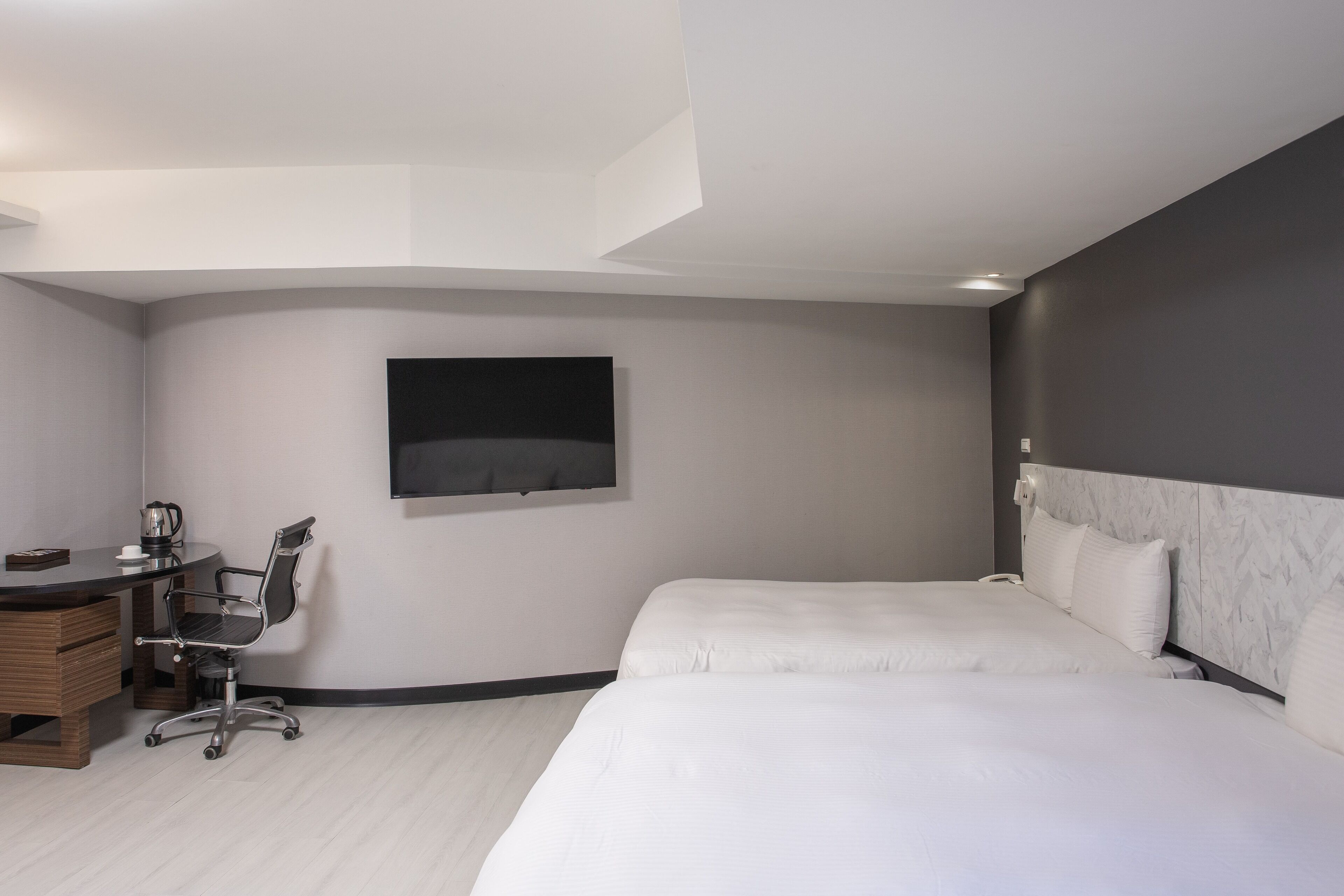 Una habitación de hotel moderna con una cama grande, un escritorio con una silla, un televisor de pantalla plana en la pared y un cabecero con diseño de mármol.