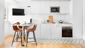 Una cocina moderna con armarios blancos, un microondas, un horno y una zona de comedor con dos taburetes.