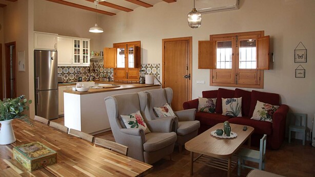 Ein gemütliches Wohnzimmer mit einem Holzespeisetisch, einem roten Sofa und einer Küchenzeile mit Holzschränken und einem Kühlschrank.