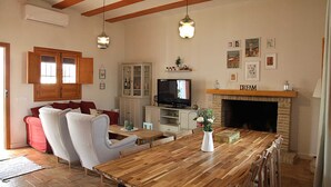 Ein Wohnzimmer mit einem Holzesstisch, zwei Sesseln, einer Couch, einem Fernseher, einem Kamin und einer Vitrine mit Glastüren.