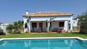 Ein zweigeschossiges Haus mit einem Ziegeldach, einem Swimmingpool und Sitzgelegenheiten im Freien.