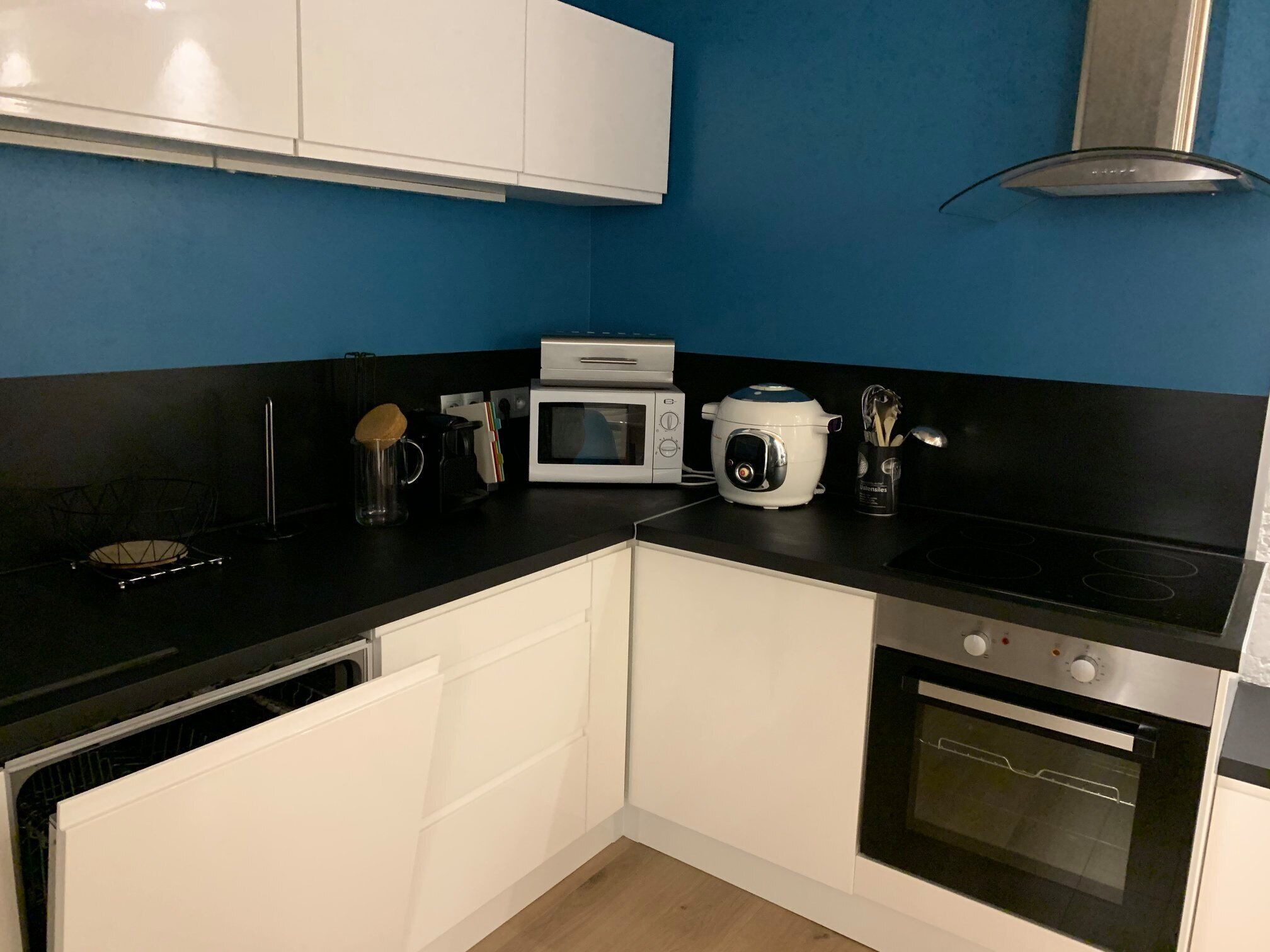 A kitchen with white cabinets, a black countertop, a microwave, a slow cooker, and an oven.