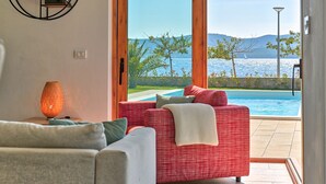 A modern living room with a red sofa, a grey sofa, and a floor lamp. There is a large window with a view of a pool and the sea. - Villa Roberta (Sveti Filip i Jakov)
