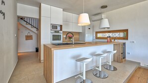 A modern kitchen with white cabinetry, a wooden island with bar stools, a built-in oven, and a window above the sink. - Villa Roberta (Sveti Filip i Jakov)