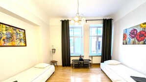 Une chambre avec deux lits simples, une petite table, une chaise, un luminaire suspendu et deux fenêtres avec des rideaux.