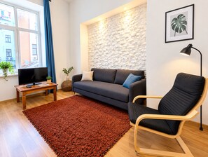A living room with a sofa, a chair, a TV, a small table, and a plant.