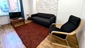 Un salon avec un canapé noir, une table basse en bois, un téléviseur, un tapis rouge et un mur en pierre.